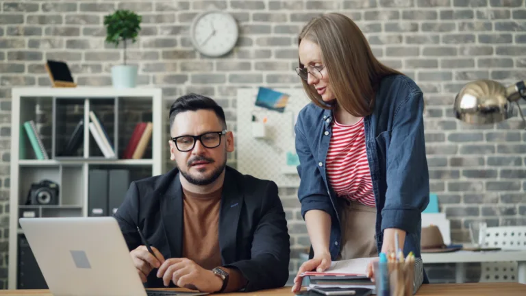 Two colleagues reviewing a website together on a laptop in a bright office, representing a collaborative website audit review